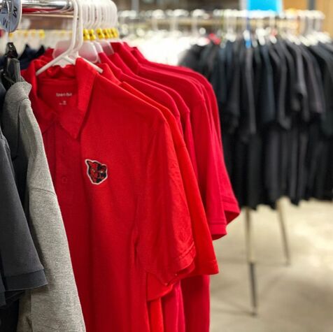 Red polo shirts are hanging on a circular rack. There is emphasis on a red shirt that contains a Petal panther logo.