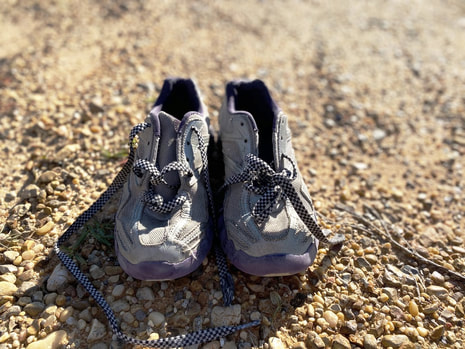 A pair of little girl's, torn up shoes placed outside in rocks. 