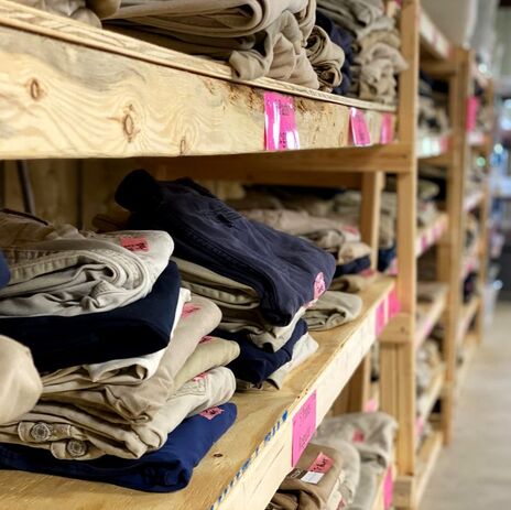 Khaki and Navy pants are stacked neatly on wooden shelves.
