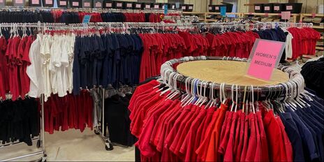 Uniform polo shirts are organized by color on both circular clothing racks and long standing clothing racks.
