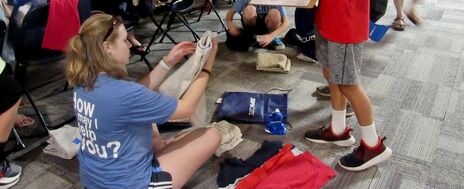 A volunteer sits on the floor folding uniforms as the family waits patiently to receive them.